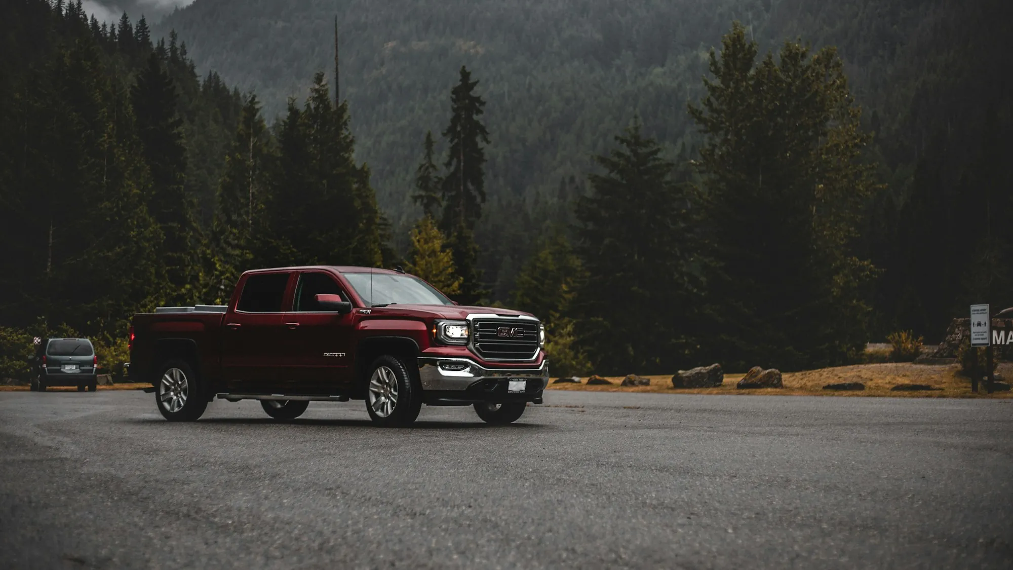 Red pickup truck parked by a forest at the edge of a mountain road